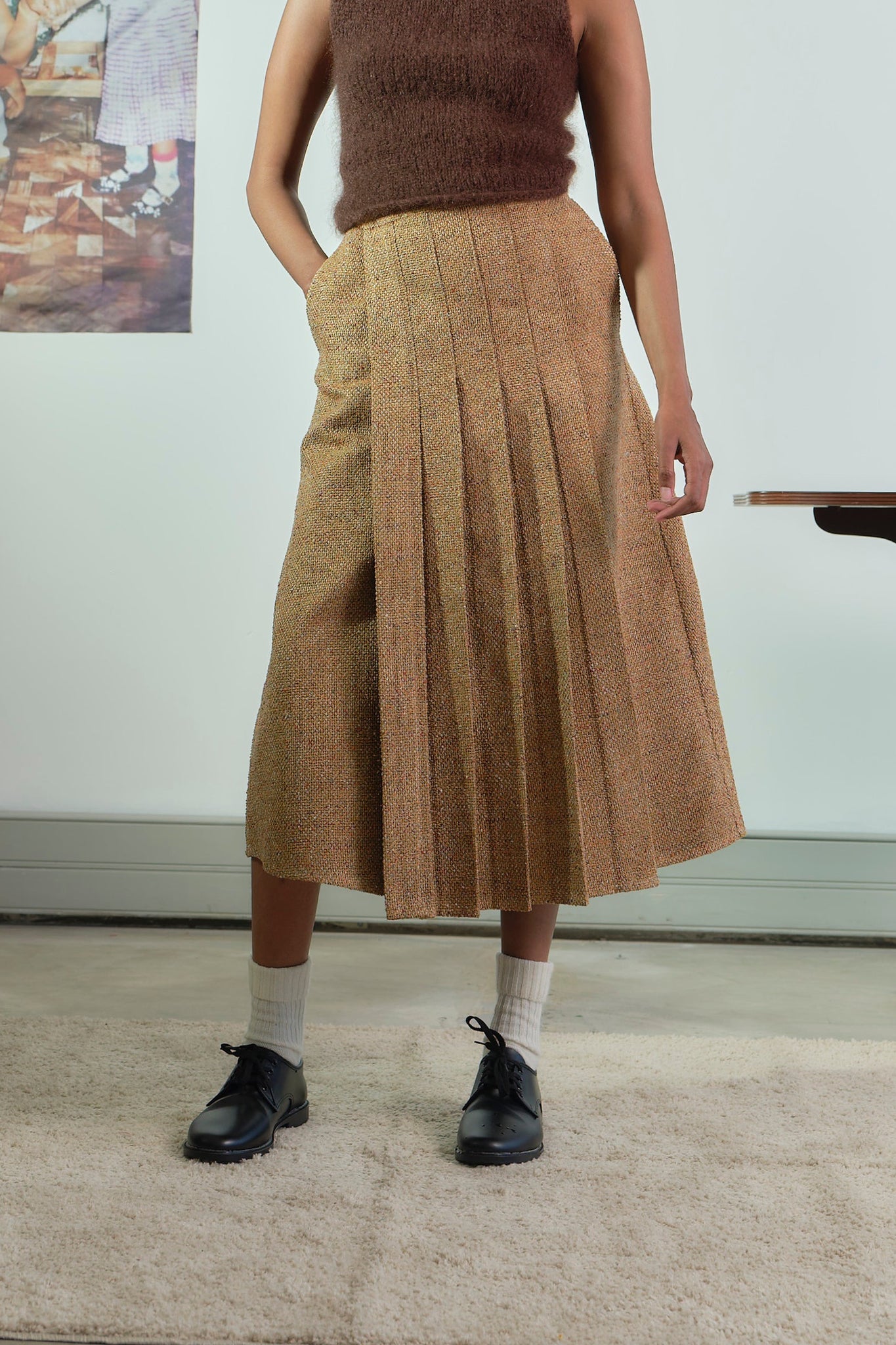 Person wearing a brown pleated skirt and brown top indoors.