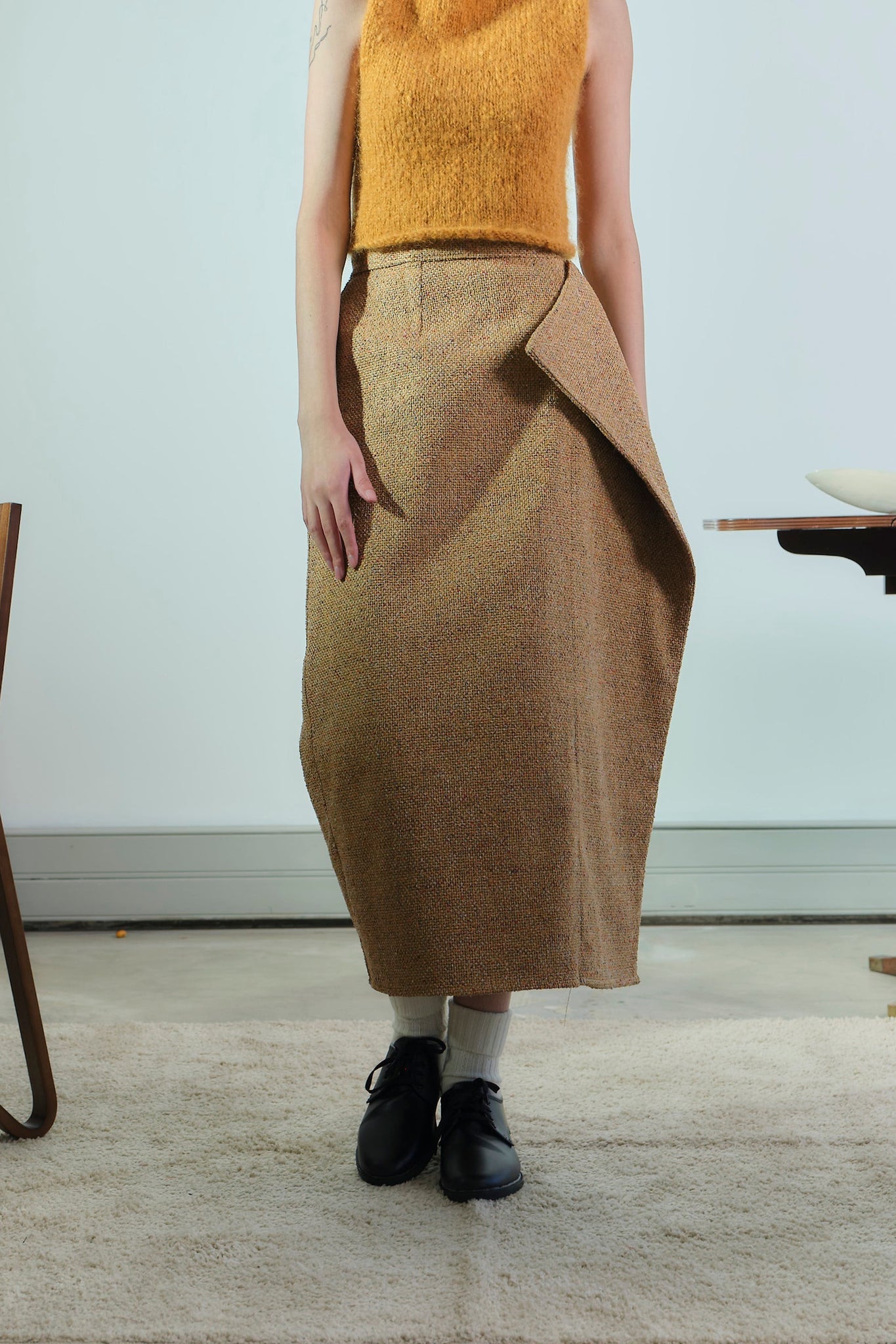 Person wearing a mustard yellow top and brown skirt in an indoor setting