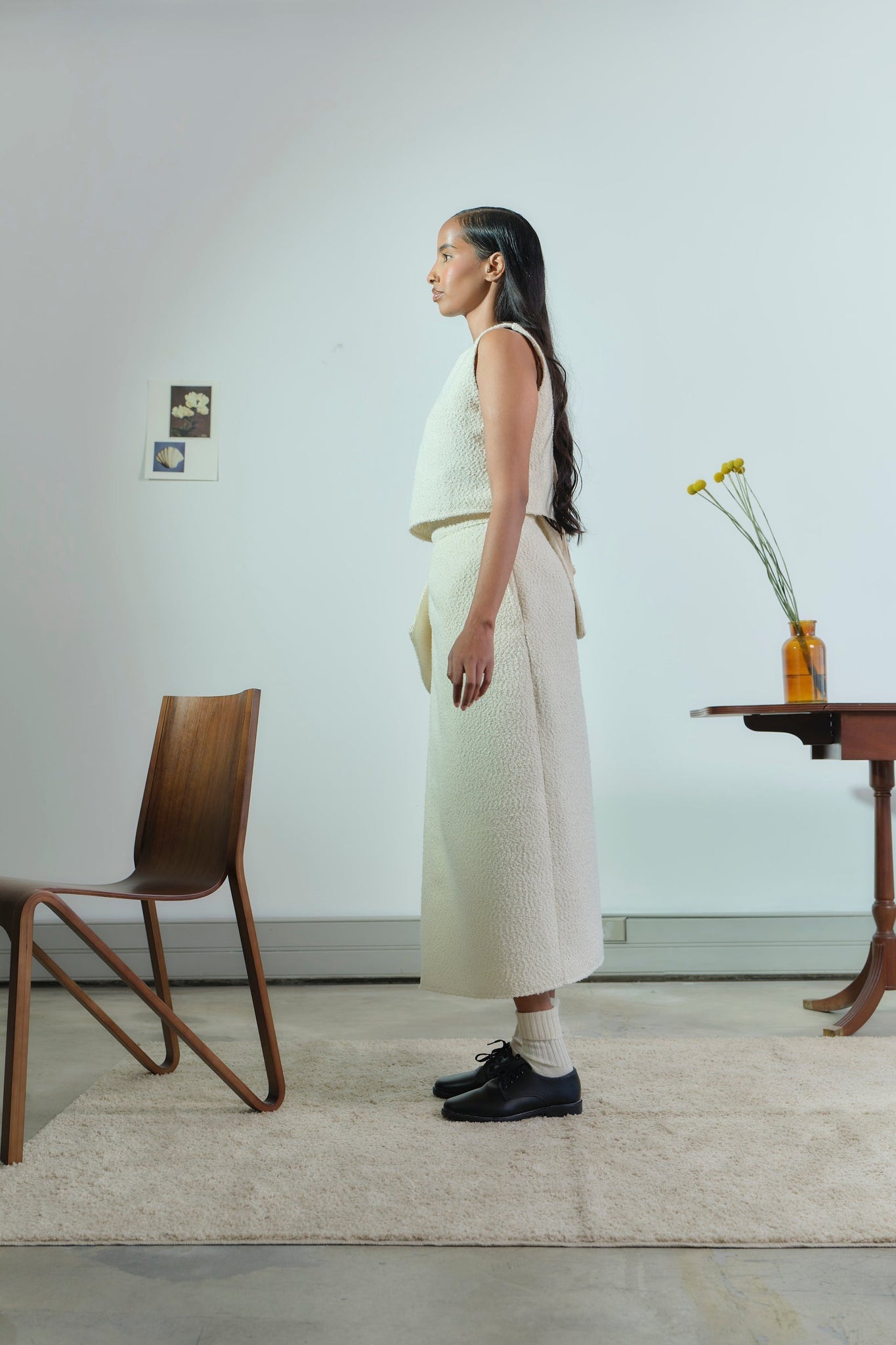 Woman standing in a minimalistic room with wooden chair and table.